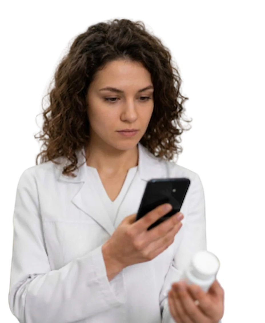 A pharmacist with curly hair looking at a smartphone while holding a medicine bottle in a pharmacy.