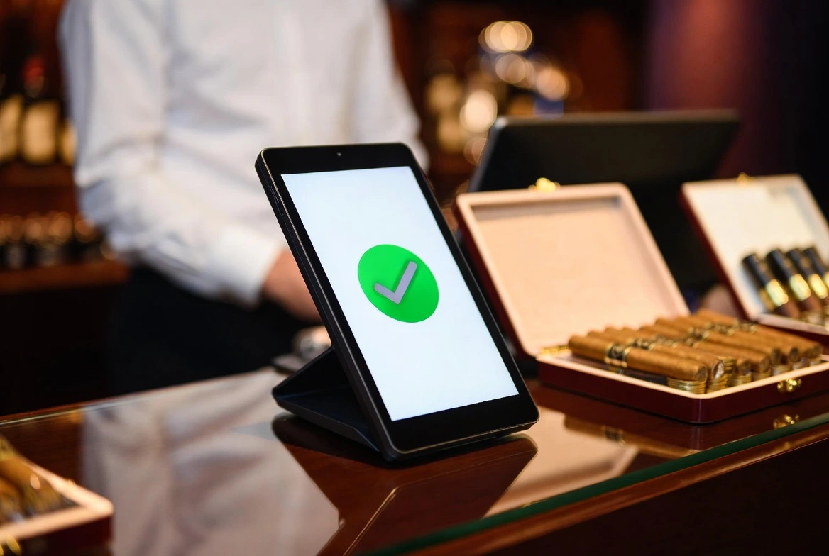 A sleek black tablet-style POS payment terminal stands on a glossy dark wooden counter